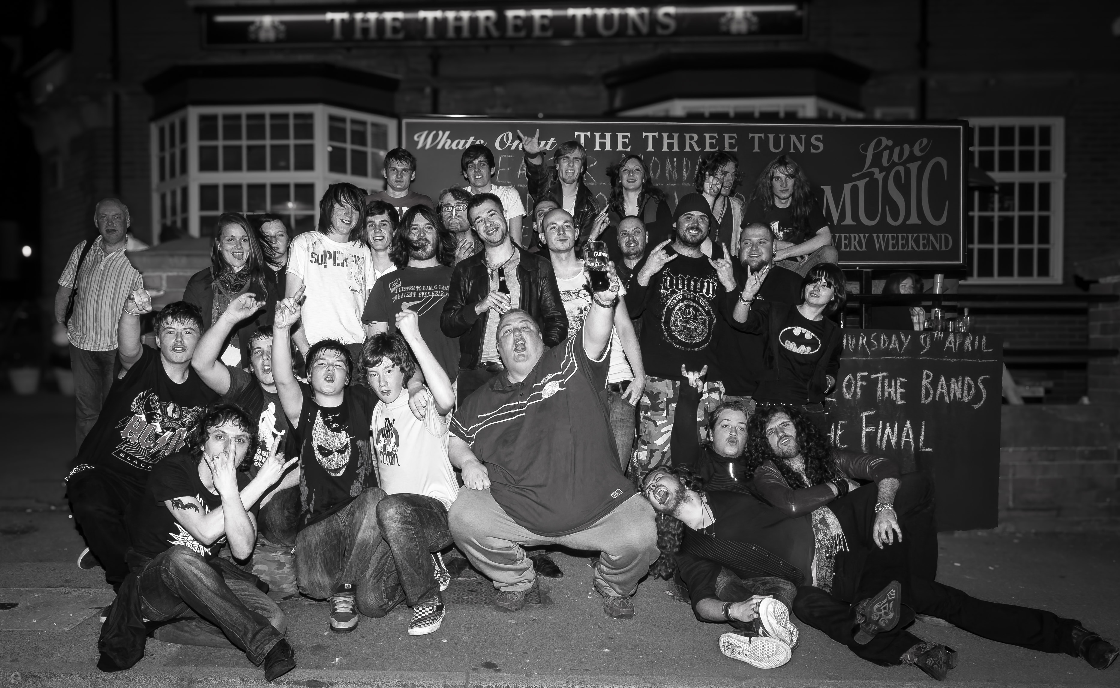 Battle of the Bands group gathered outside The Three Tuns pub beneath live music signage