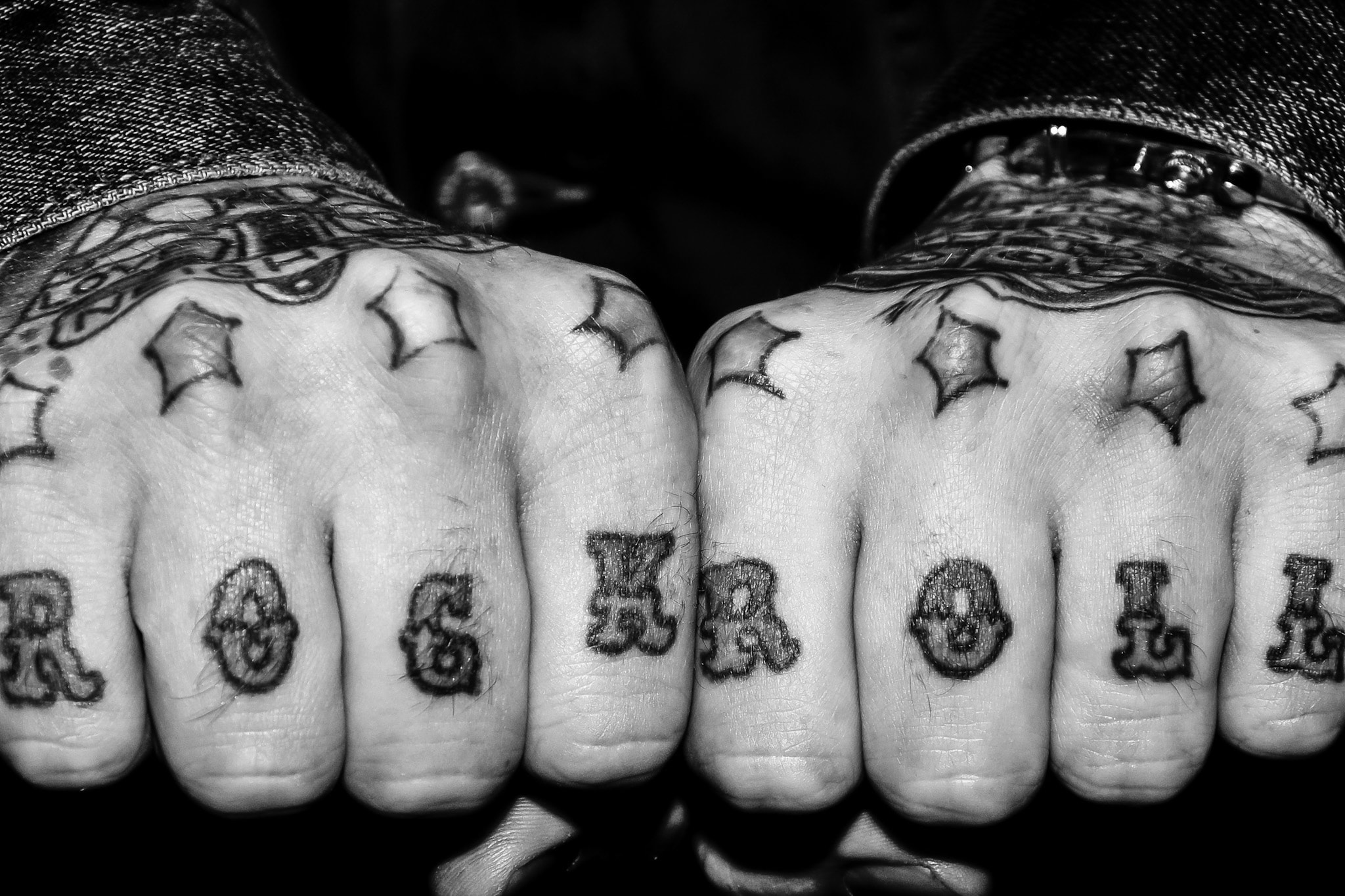 High-contrast black-and-white close-up of tattooed fists spelling Rock and Roll