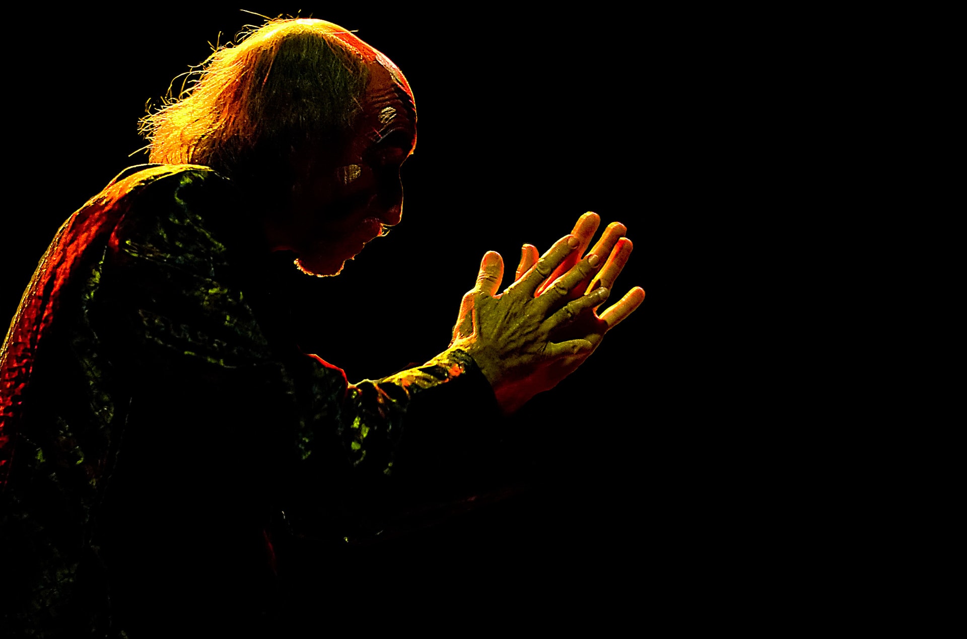 Arthur Brown performing in profile with hands raised against a dark stage background