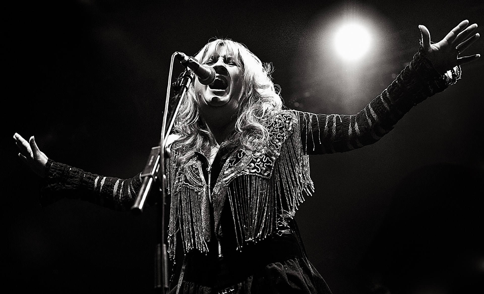 Debra Bonham singing live into a microphone in a black-and-white concert photograph