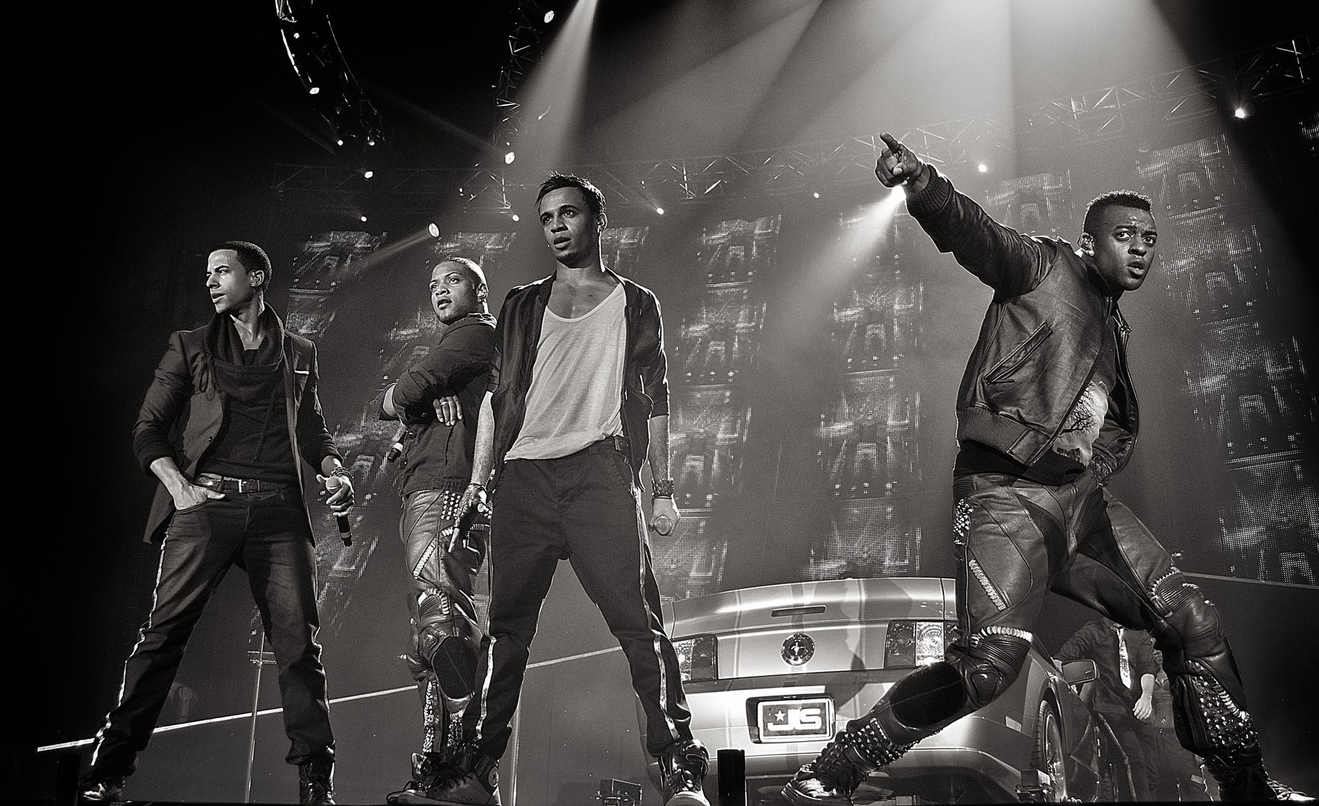 JLS performing together on stage in a black-and-white concert photograph