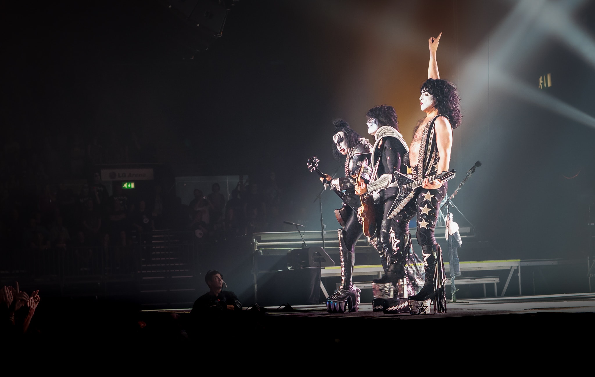 Gene Simmons, Paul Stanley and Tommy Thayer of KISS performing on stage in full costume and makeup with Paul Stanley pointing one finger to the sky during the Sonic Boom UK tour