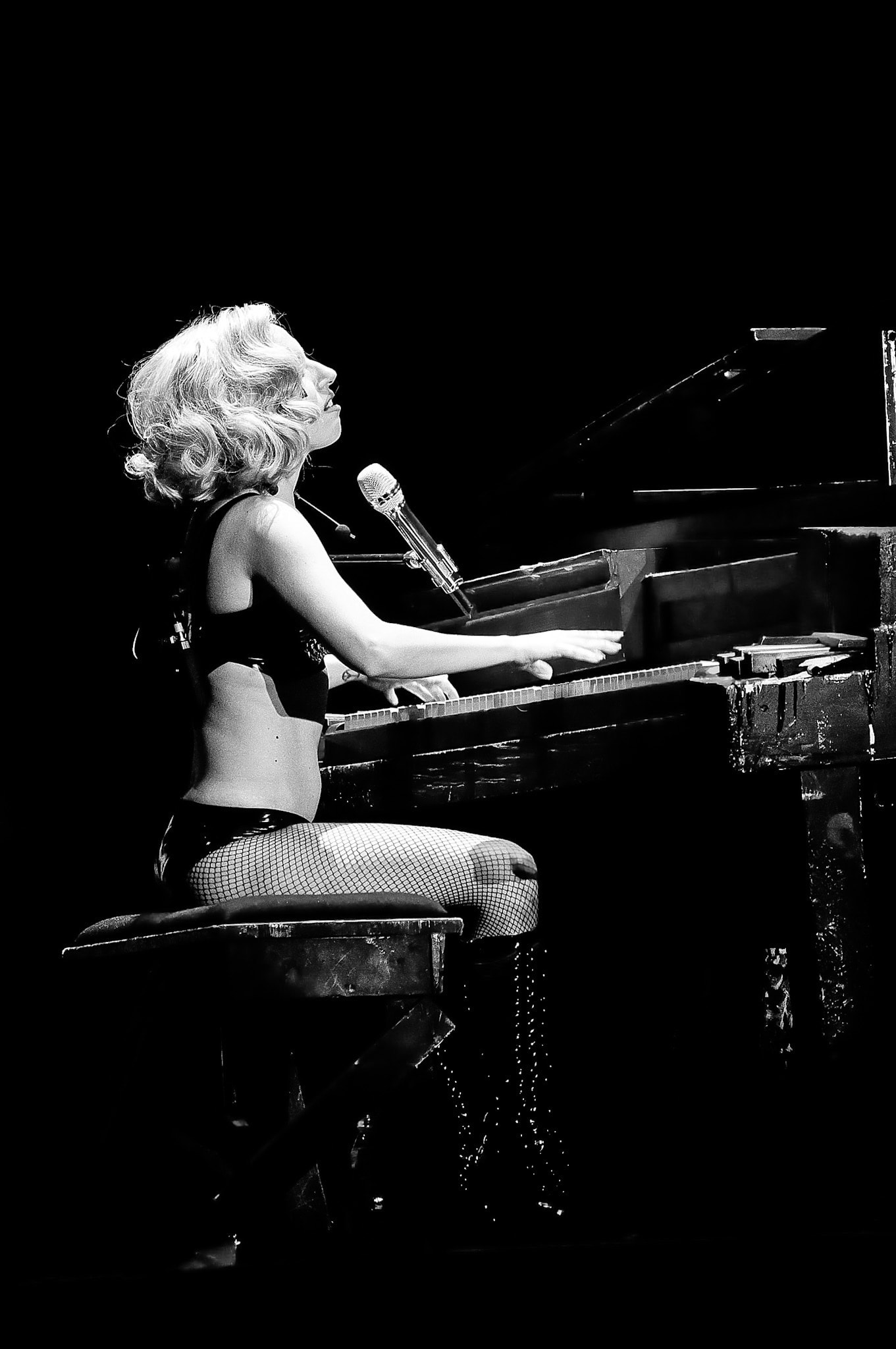 Lady Gaga playing piano and singing in a high-contrast black-and-white concert photograph