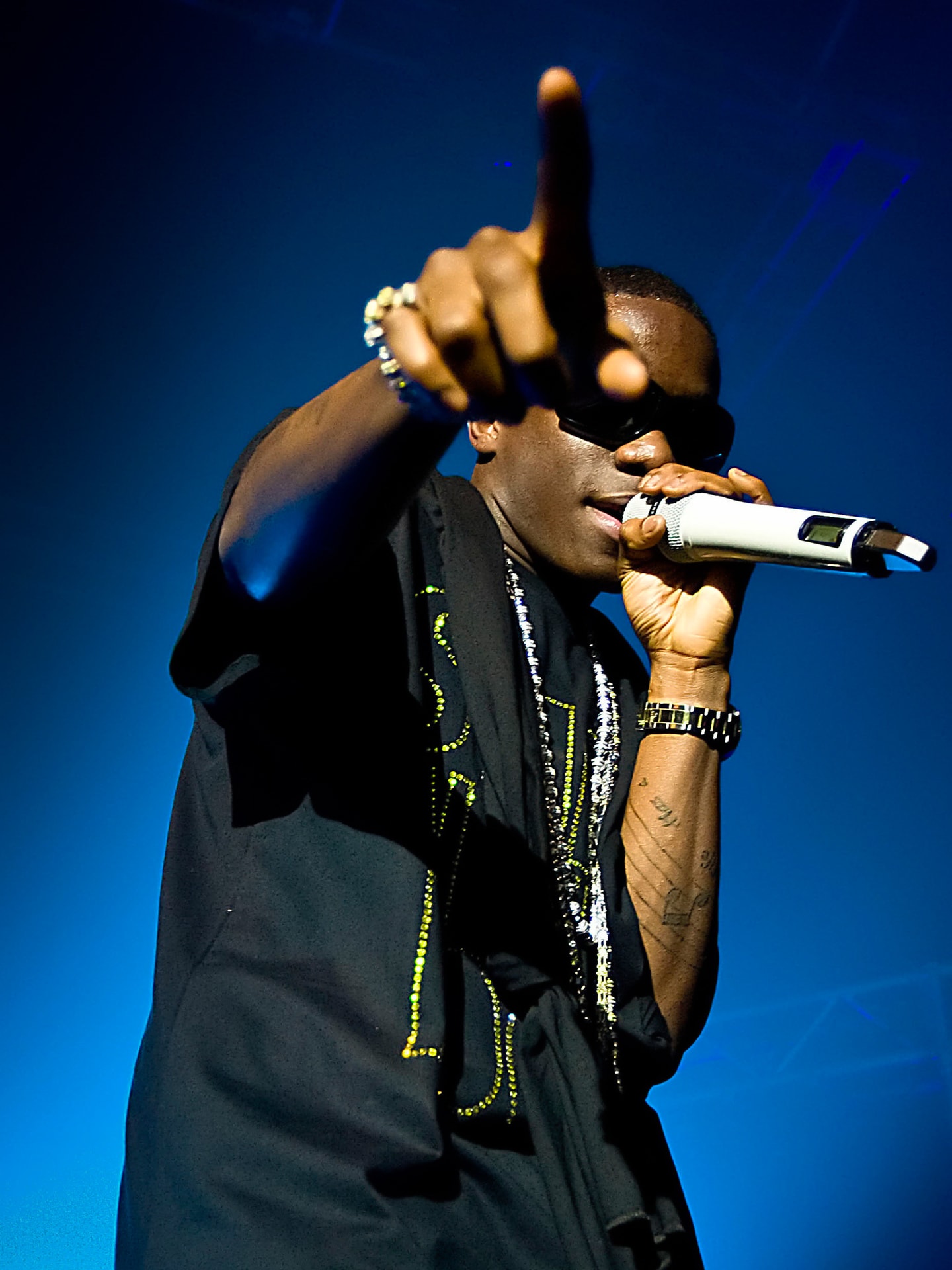 Tinchy Stryder performing live with a microphone under blue stage lighting