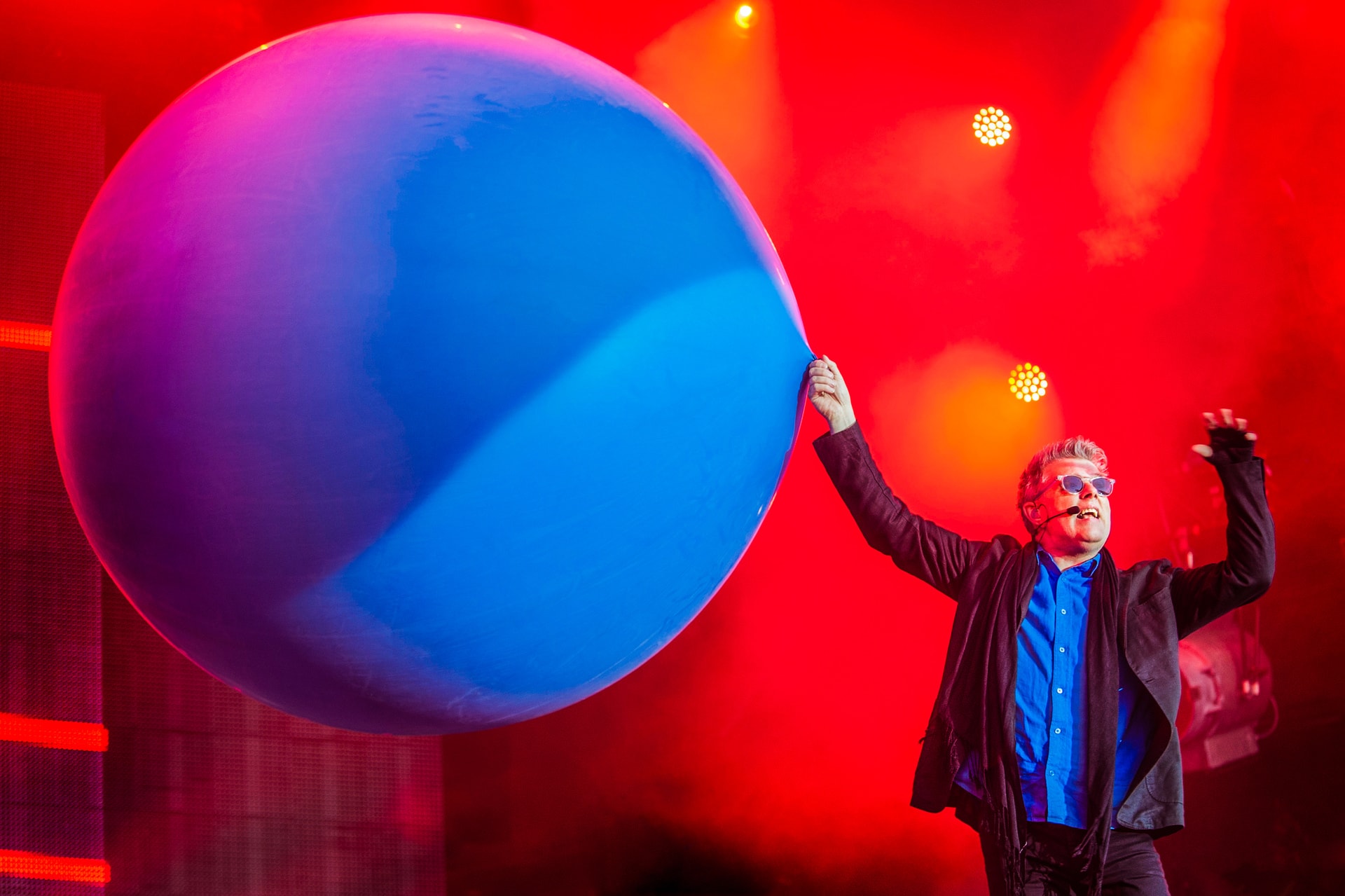 Tom Bailey of The Thompson Twins performing beside a large blue balloon under red stage lights